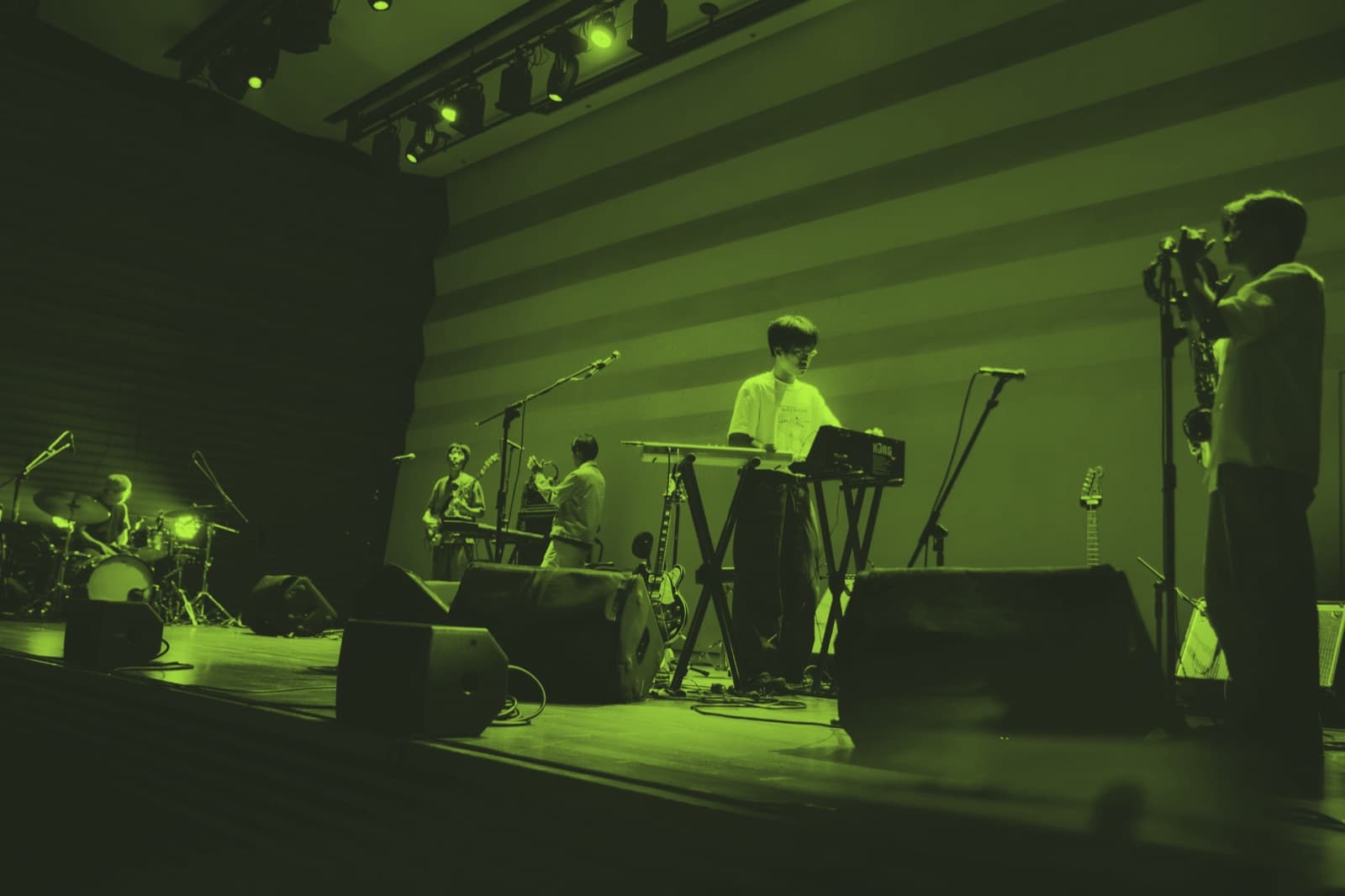 A band mid-set on a wide stage under green wash lighting