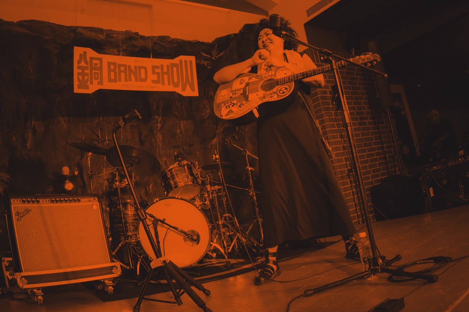 A solo guitarist on a small stage beneath a hand-painted BAND SHOW banner